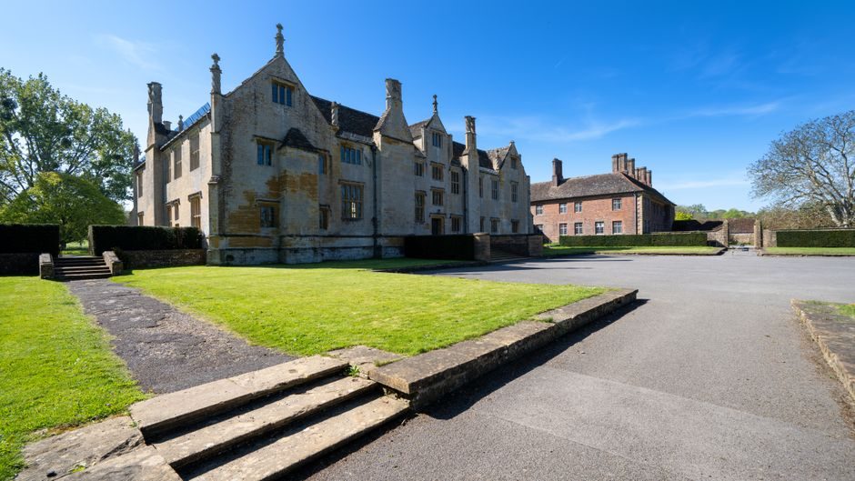 A picturesque view of a historic manor house in England basking under a clear blue sky.
