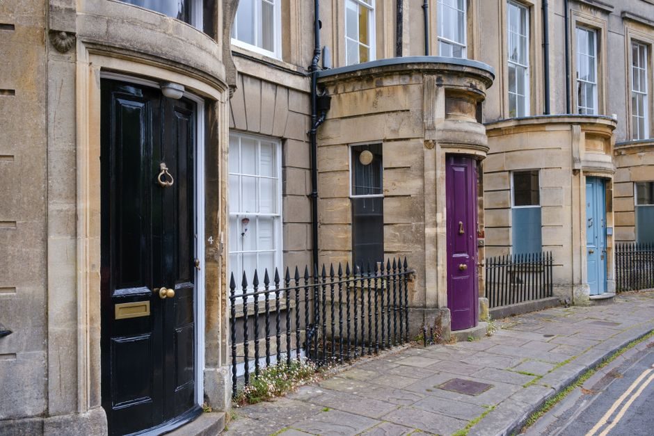 A row of vibrant Georgian-style doors on a classic British street featuring black, purple, and blue doors.