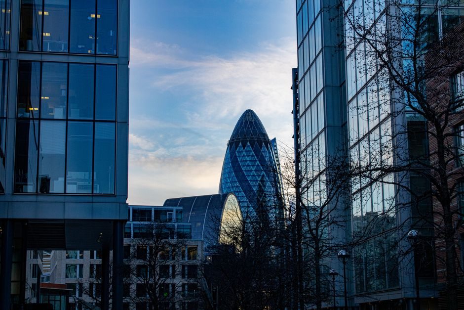 Stunning view of London's iconic Gherkin building framed by modern glass skyscrapers against a blue sky.