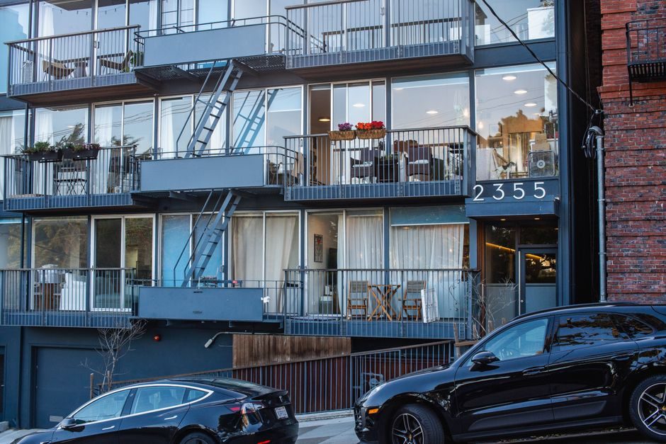 Contemporary city apartment building with glass balconies and parked cars in the foreground.