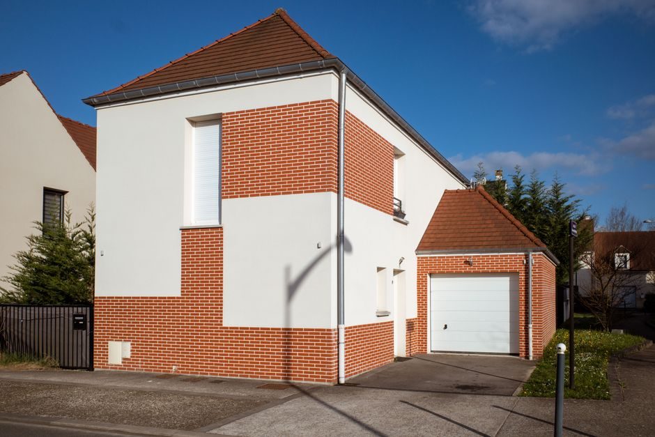 A contemporary suburban home with red brick and white facade in a sunny neighborhood setting.