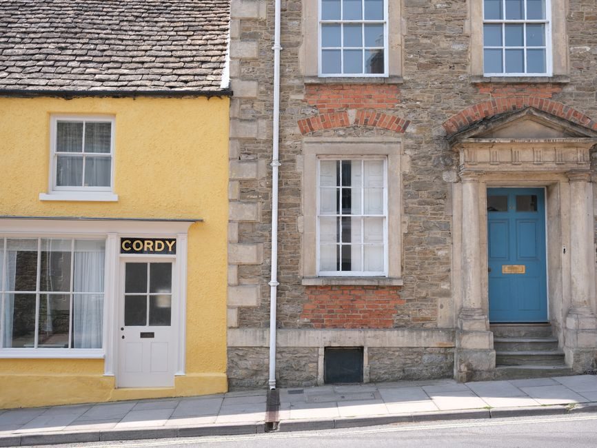 Vibrant street view of charming English village architecture featuring yellow and stone buildings.