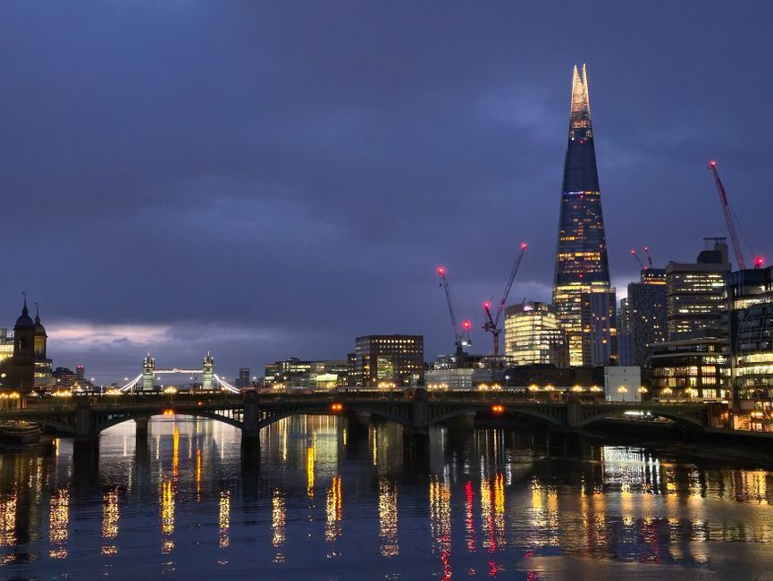 Stunning nighttime view of London's skyline, featuring the Shard and Tower Bridge reflecting in the River Thames.