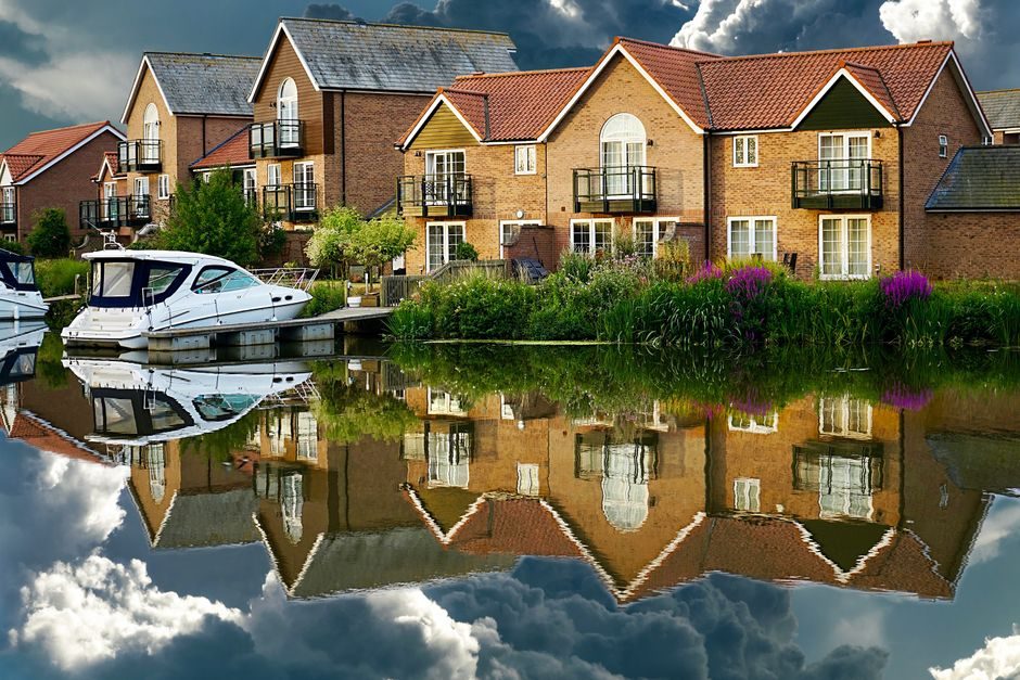 Picturesque houses and yachts reflected on a serene canal under dramatic skies.
