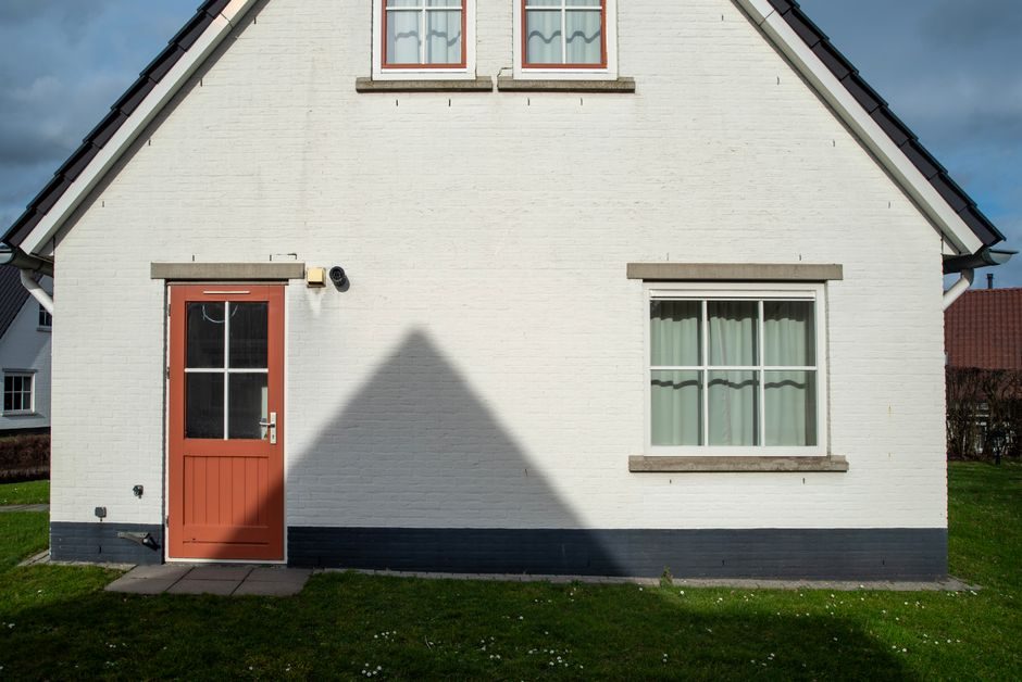 Front view of a charming house with a red door casting a shadow, under clear skies.